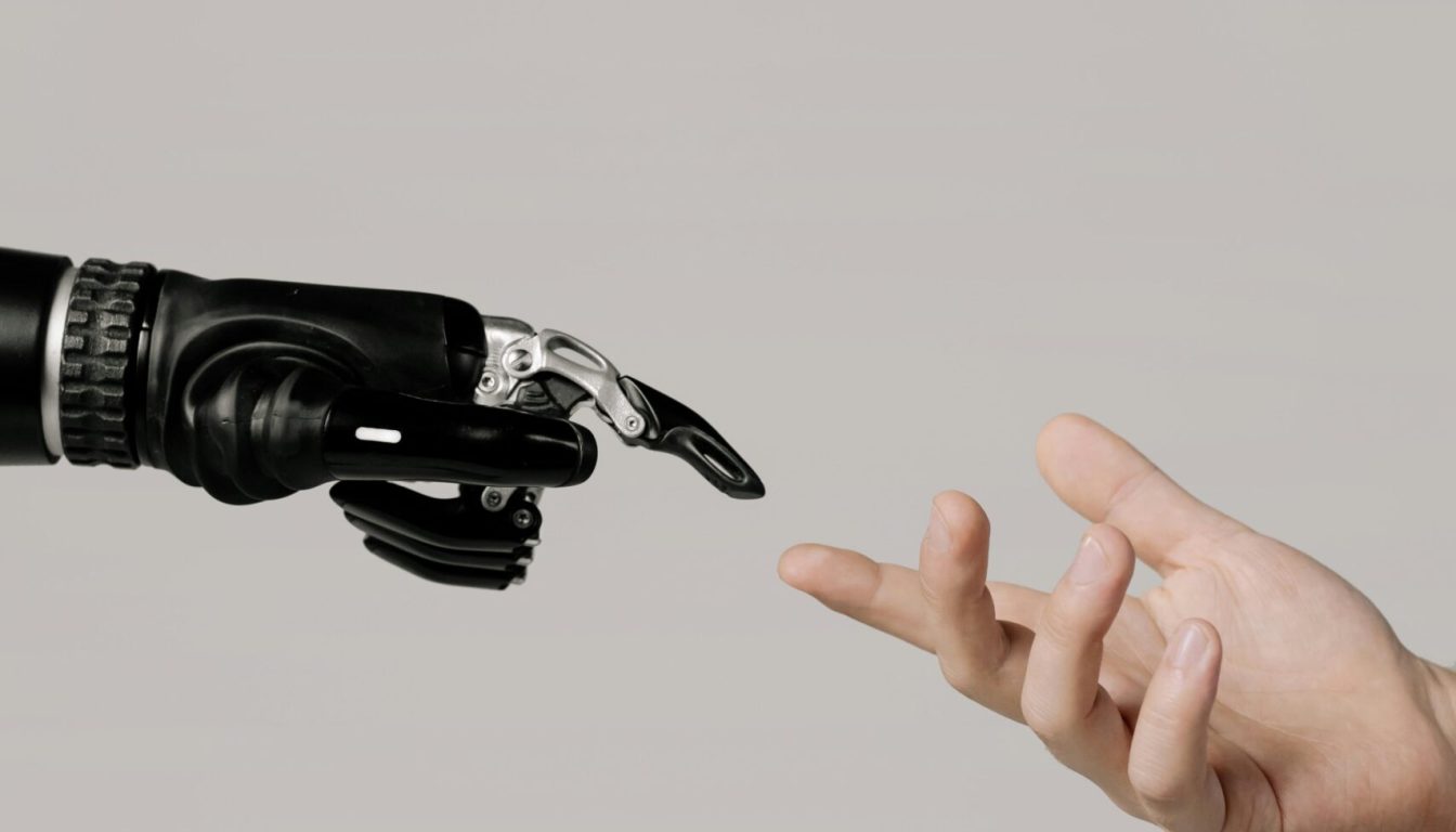 pexels-photo-6153343-6153343 A human hand reaching to touch a bionic prosthetic hand on a white background.